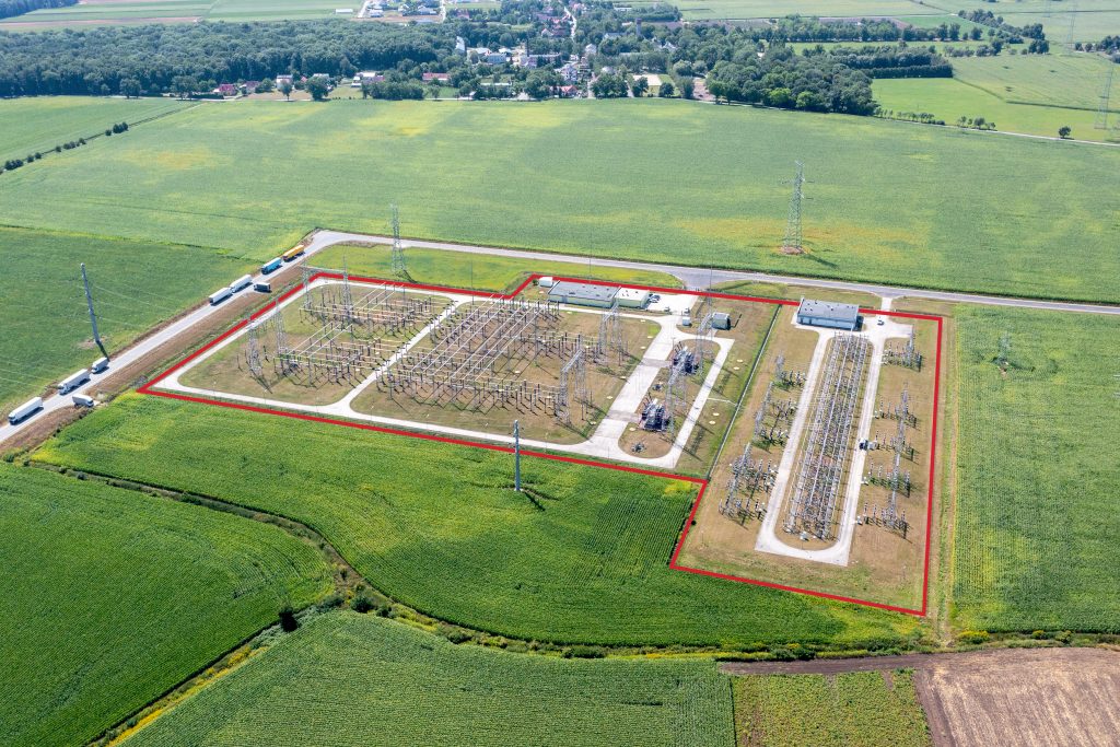 Aerial view of an electrical substation in farmland with its security perimeter marked in red